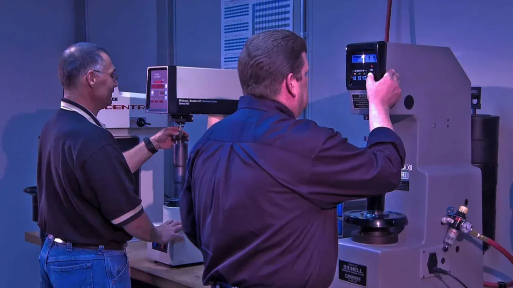 Engineers operating metal testing equipment in a quality-control laboratory